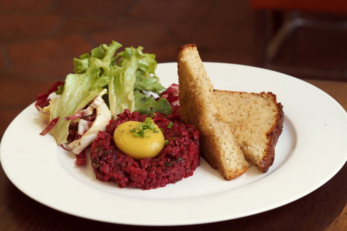 Ein Teller mit veganem Tatar aus Linsen und Roten Rüben mit pflanzlichem "Ei-Dotter", Salat und Brot.