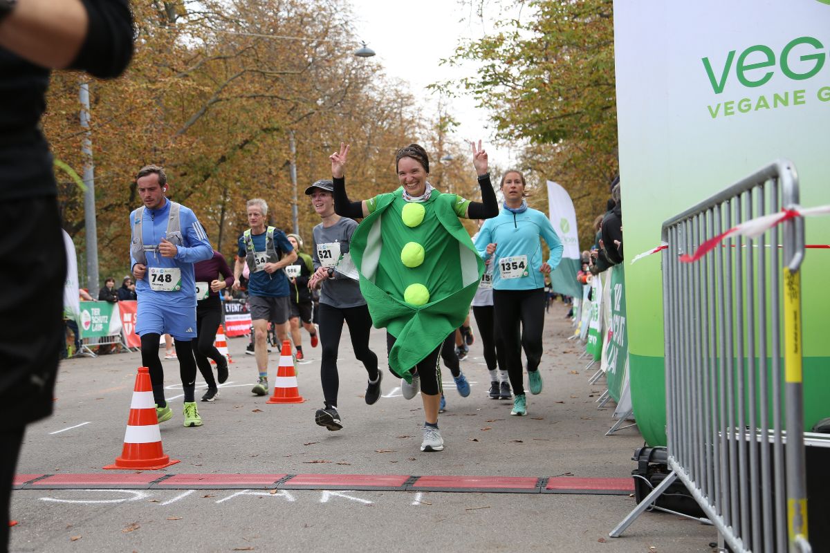 Mehrere Personen beim Zieleinlauf, vorne eine Person in einem Erbsenkostüm, die die Hände nach oben hält und grinsend ins Ziel läuft.
